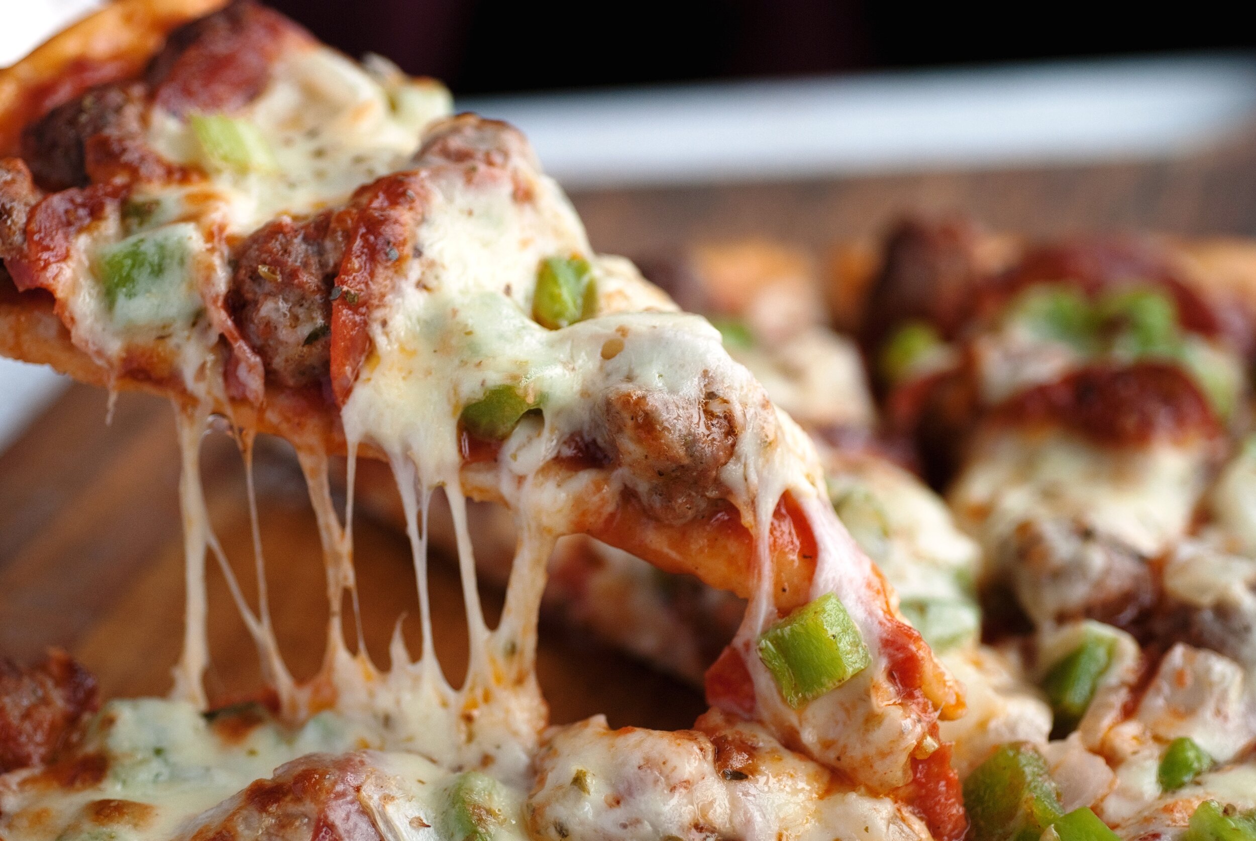 A fresh slice of cheese pizza with sausage and green pepper being served